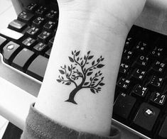 black and white photo of a tree tattoo on the left wrist by a computer keyboard