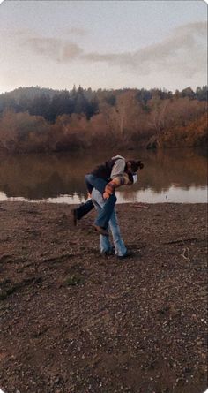 two people are playing in the mud near a body of water with trees in the background