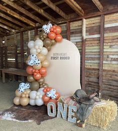 an arch made out of balloons and some hay is sitting in front of a sign that says first rodeo