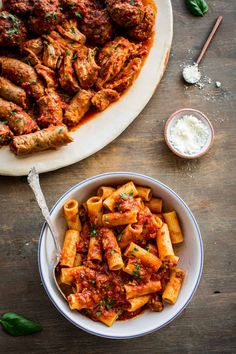 pasta with meatballs and sauce in a bowl on a wooden table next to a platter