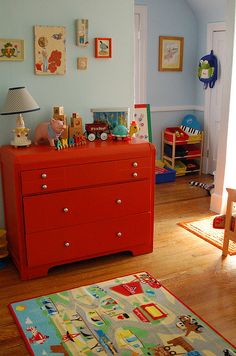 a child's bedroom with blue walls and wooden floors, including a red dresser