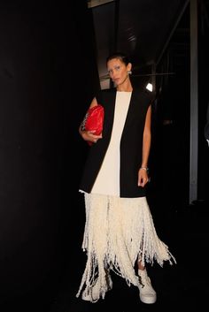 a woman in a white dress and black jacket is holding a red purse while walking