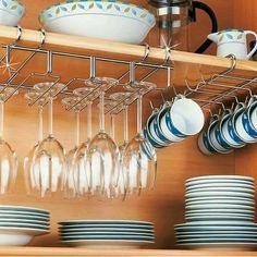 wine glasses and plates are hanging on the rack in this kitchen cabinet with wooden shelves