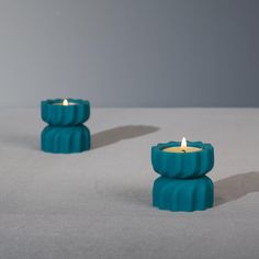 two teal colored candles sitting on top of a gray table next to each other