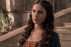 a woman standing in front of some steps wearing a necklace and brown dress with long curly hair