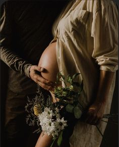 a pregnant woman holding a bouquet of flowers next to a man in a brown shirt