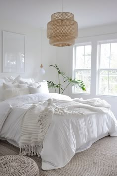 a bed with white linens and pillows in a room next to two large windows