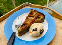 a piece of cake and ice cream on a blue plate with a wooden tray in the background