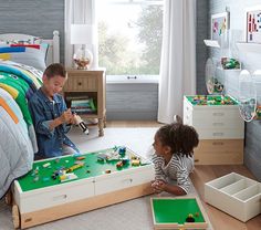 two children playing with legos in a bedroom setting, one boy is sitting on the floor