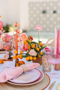 the table is set with oranges and pink flowers in vases, plates and napkins