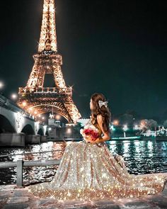 a woman in front of the eiffel tower at night with lights on her dress