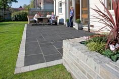 people are sitting outside on the patio in front of their house, while one person is standing