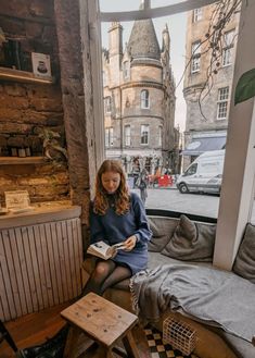 a woman sitting on a window sill reading a book