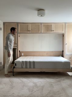 a man standing next to a bed in a room with white carpet and wooden cabinets