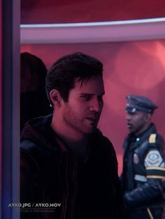 a man standing next to another man in a room with red lights and police officers