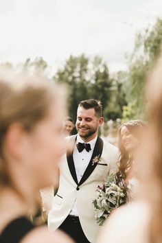 a man in a tuxedo smiles as he walks down the aisle with his bride