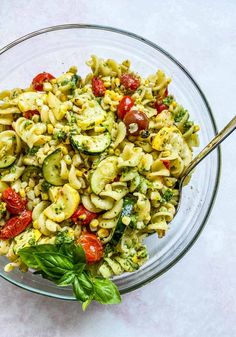 a glass bowl filled with pasta salad on top of a white table next to a silver spoon