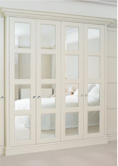 a white bedroom with mirrored doors on the wall