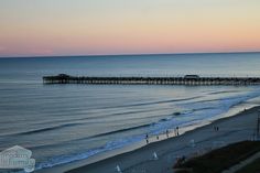 the ocean and pier at sunset with people walking on the beach