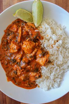 a white plate topped with rice and meat next to a slice of green leafy lime