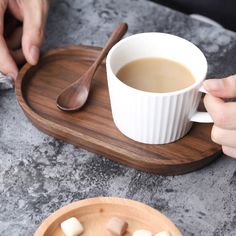 a cup of coffee and some marshmallows on a wooden tray with two hands