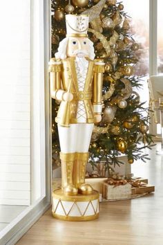 a gold and white nutcracker standing next to a christmas tree in front of a window