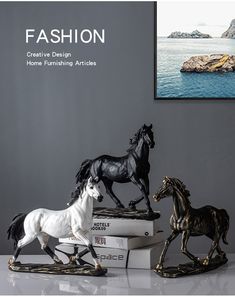 three horse figurines sitting on top of books in front of a gray wall