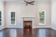 an empty living room with a fireplace and two windows