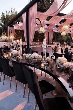 a long table with black chairs is set up for an outdoor wedding reception in the evening