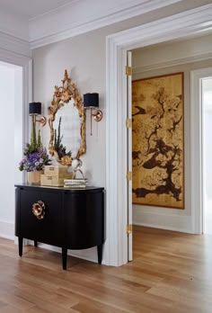 a room with a black cabinet, mirror and flowers on the table in front of it