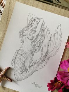 a drawing of a mermaid sitting on top of a wooden table next to pink flowers