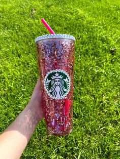 a hand holding a red starbucks cup with glitter on it and a straw sticking out of the lid