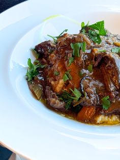 a white plate topped with meat covered in sauce and garnished with parsley