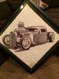 a drawing of an old car is displayed in a frame on the floor next to a couch