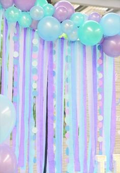 balloons and streamers are hanging from the ceiling in front of a party backdrop with pastel colors