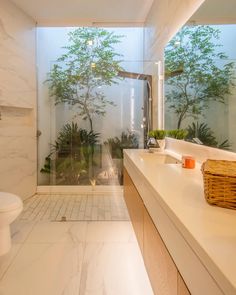 a bathroom with a glass shower door and white counter top next to a toilet in front of a window