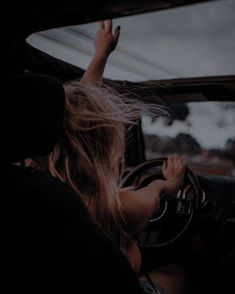 a woman sitting in the driver's seat of a car with her hand on the steering wheel