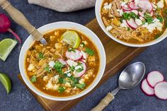 two bowls of soup on a cutting board with radishes and limes next to it