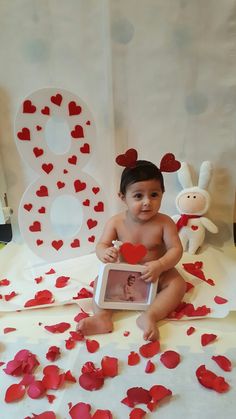 a baby is sitting on the floor with hearts scattered around him and holding a photo frame