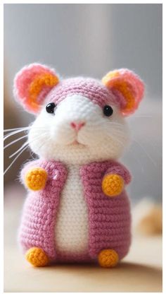 a small crocheted mouse wearing a pink and yellow sweater with orange buttons on it's chest