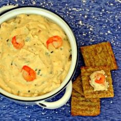 a bowl of hummus with crackers and carrots next to it on a blue surface