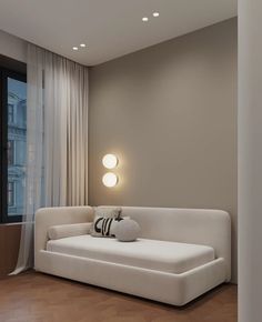 a white couch sitting in front of a window next to a wall mounted light on a wooden floor