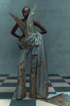 a woman standing in front of a checkered floor wearing a gray and gold dress