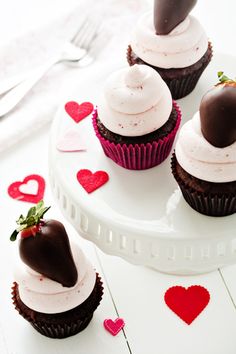 chocolate cupcakes with white frosting and strawberries on top, surrounded by hearts