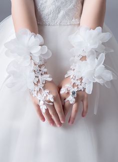 a woman in a wedding dress holding her hands with white flowers on the wrist and cuffs