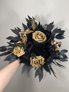 a bridal bouquet with black and gold flowers is being held by a woman's hand