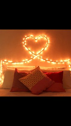 a bed with lights on the headboard and pillows in front of it that are shaped like a heart