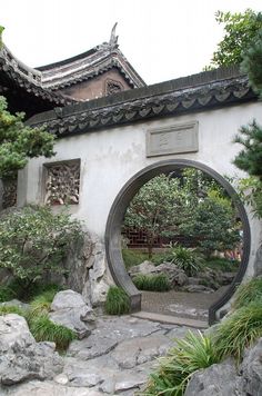 an arch in the middle of a garden with rocks and plants around it, surrounded by greenery