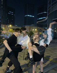 three people posing for a photo in front of some buildings at night with their arms up