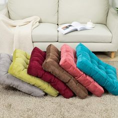 a pile of pillows sitting on the floor in front of a couch with a book